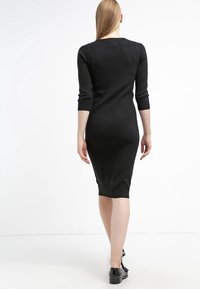 Svart stickad klänning med trekvartsärmar, åtsittande form, ribbade muddar och fåll, slät textur, når under knäet.