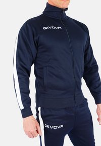 Mornarska zip-up trenirka iz gladkega materiala, s prečnimi belimi črtami na rokavih, stranskimi žepi in belim logotipom "GIVOVA" na prsih.