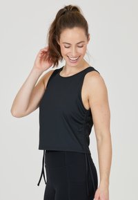 Top sportivo nero a maniche corte con texture a costine, dettagli arricciati sui lati e lacci regolabili. Abbinato a leggings neri a vita alta.