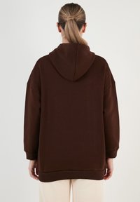 Barna, oversized kapucnis pulóver, húzózsinórral, hosszú ujjakkal és bordázott mandzsettákkal, puha, tekstúrált anyagból készült. Tiszta, egyszerű dizájn.