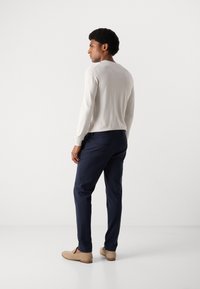Lichtgrijze lange mouwen trui, marineblauwe broek en beige instappers. Gladde textuur, slim fit ontwerp met subtiele schoudernaaddetails.