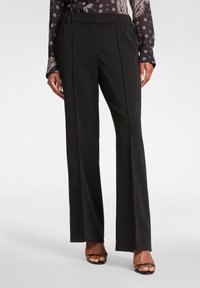 Czarne spodnie o prostym kroju z gładką fakturą i paskiem w talii. Mają plisowany krój i sięgają do kostek, zestawione z czarnymi sandałami na paski.