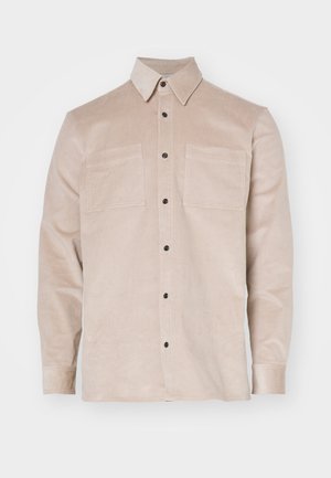 Beżowa koszula z korduroju z kołnierzykiem zapinanym na guziki, z dwoma przednimi kieszeniami i czarnymi guzikami. Miękka tekstura i klasyczny design.