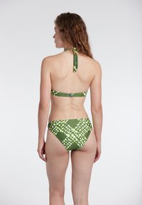 Zeleno bikinij s halter vrvico; vzorec vsebuje svetlo zelene oblike. Zgornji del ima zaklep, spodnji del pa se nosi na srednjem pasu.