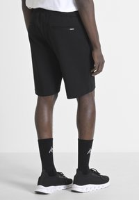 Shorts sportivi neri con cintura elastica, tessuto liscio e una tasca posteriore. Abbinati a calzini neri alla caviglia e scarpe da ginnastica nere con suola bianca.