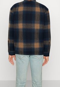 Marineblauw en oranje geruit shirt met een relaxte pasvorm, knopenmanchetten en een rechte zoom. Gemaakt van zachte stof, weergegeven vanuit de achterkant.