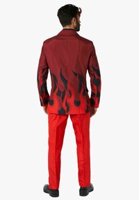 Chaqueta de traje roja con patrones de llamas negras, combinada con pantalones rojos. La chaqueta presenta una textura suave y un diseño ajustado. Cuello clásico y botones.