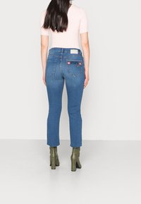 Blå denimjeans med en åtsittande design, prydda med blommig broderi på bakfickorna och en kortare skärning ovanför anklarna.