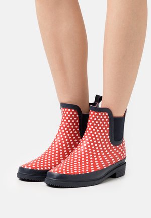 Botas de lluvia rojas hasta el tobillo, hechas de goma, con lunares blancos, paneles laterales elásticos negros y suelas texturizadas negras.