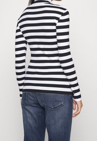 Svart och vit randig långärmad topp med hög halsringning, ihop med blå jeans. Bomullsmaterial, figurnära silhuett och ribbat mönster.