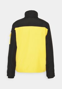 Czarna i żółta kurtka z wysokim kołnierzem. Żółta część główna z czarną górną częścią i rękawami, z kieszenią po boku. Gładka tekstura.