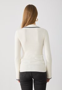 Ribbed long-sleeve top in off-white with navy accents along the collar and cuffs. Body-hugging fit and smooth texture. Design emphasizes simplicity.