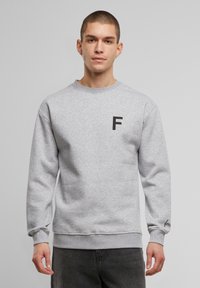 Hall vest, mille halli ja ümara kaelusega, mille esithelmel on must "F" logo ja manseti peal tikand. Sile tekstuur, mugav lõige.