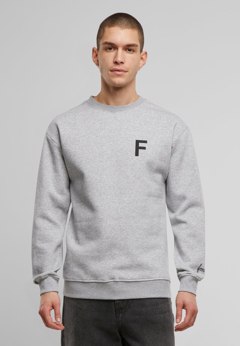 Hall vest, mille halli ja ümara kaelusega, mille esithelmel on must "F" logo ja manseti peal tikand. Sile tekstuur, mugav lõige.