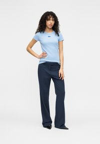 Ανοιχτό γαλάζιο εφαρμοστό μπλουζάκι με κοντά μανίκια και μικρό λογότυπο, συνδυασμένο με σκούρο μπλε ραμμένο παντελόνι και μαύρα παπούτσια με μυτερή μύτη.