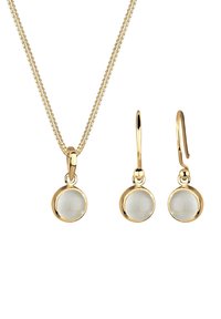 Ensemble de bijoux en ton doré comprenant un collier avec pendentif et des boucles d'oreilles assorties, chacune ornée d'une pierre blanche circulaire encastrée dans un sertissage doré.
