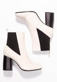 Bílé a černé kotníkové boty s geometrickým designem, texturovaný kožený a textilní svršek a silný černý podpatek.