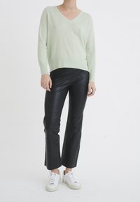 Pull vert clair à col en V avec ourlet côtelé, associé à un pantalon noir en similicuir taille haute et des baskets blanches avec des accents gris.
