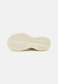 Semelle de basket en caoutchouc blanc cassé, avec un motif de semelle texturé comportant des rainures et un design angulaire pour une meilleure adhérence. Logo de la marque visible.