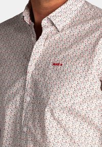 Witte overhemden met een klein bladpatroon in groen, rood en grijs. Bevat een zak met een geborduurd logo op de borst.