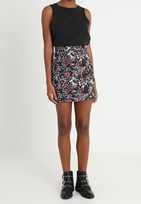 Top negro sin mangas combinado con una falda corta floral de fondo oscuro, patrones coloridos y botas negras hasta el tobillo con tachuelas plateadas.