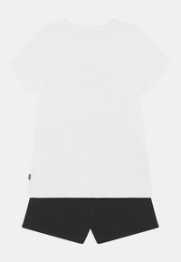 Camiseta de algodón blanca con mangas cortas, combinada con pantalones cortos negros. Ambos son sencillos en diseño, con un ajuste clásico y sin patrones visibles.
