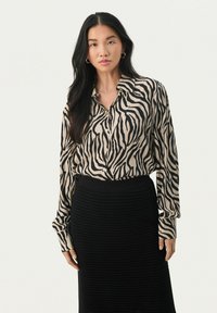Beige bluse med sorte zebra-striber, med knaplukning, krave og lange ærmer. Sat sammen med en struktureret sort strikskørt.
