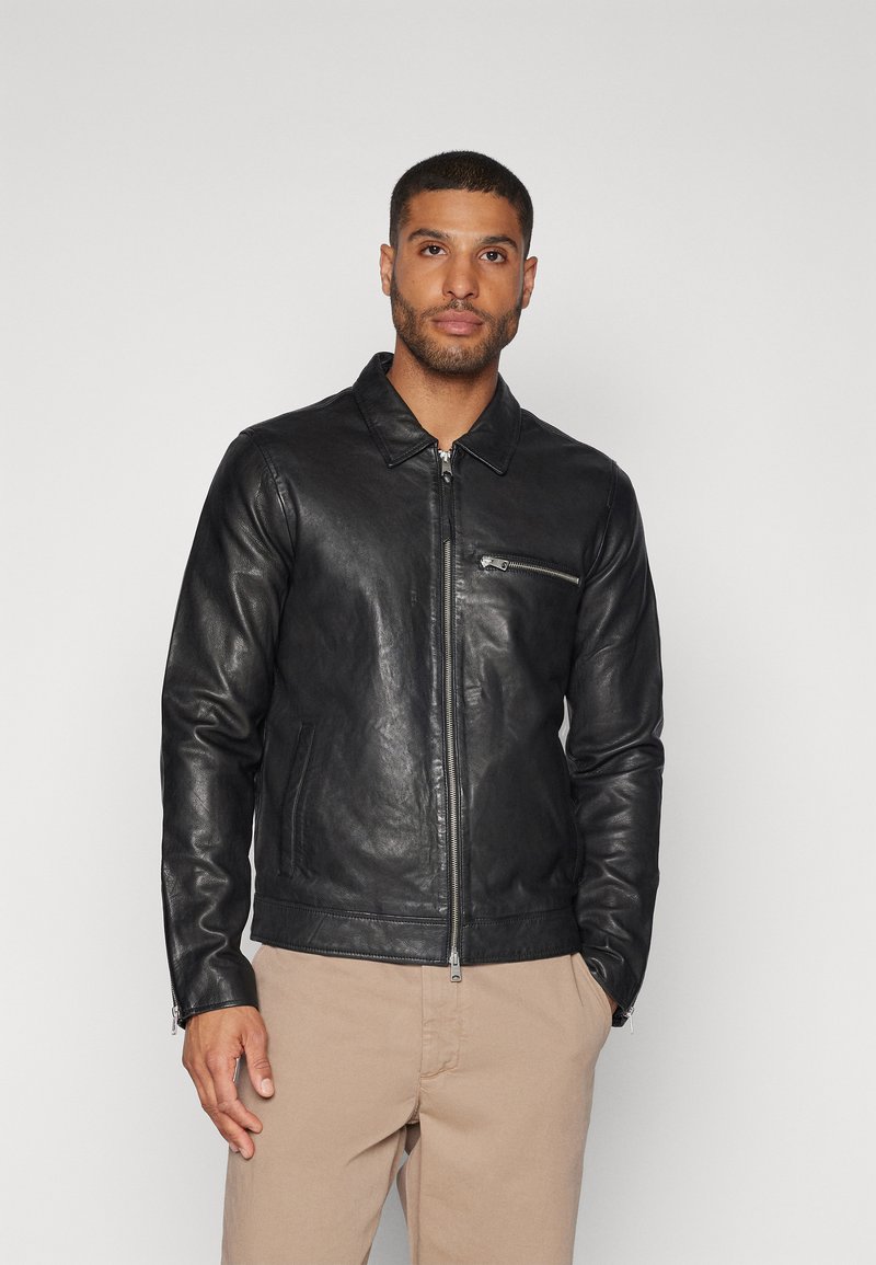 Schwarze Lederjacke mit Kragen, Frontreißverschluss und einer kleinen Brusttasche. Glatte Textur und schmaler Schnitt mit minimalem Hardware-Einsatz.