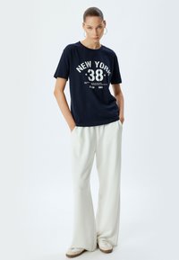 Camiseta de algodón navy con impresión blanca "NEW YORK 38", combinada con pantalones anchos blancos, que presentan un corte relajado y una textura suave.