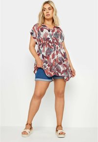 Túnica con estampado floral en blanco, rojo y azul marino, con mangas cortas y escote en V, combinada con shorts de mezclilla y sandalias espadrilles.