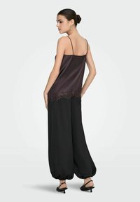 Saténový top bez rukávů v tmavě hnědé barvě s krajkovým lemem, zkombinovaný s černými širokými kalhotami s elastickými manžetami a černými sandály na pásky.