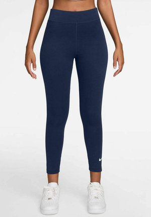 Leggings azul marino hechos de tejido elástico, diseño de cintura alta, con un pequeño logotipo blanco de Nike cerca del tobillo, textura suave.