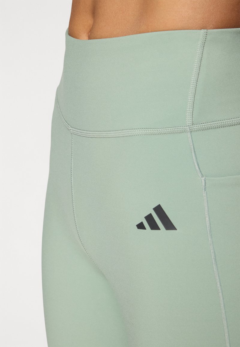 Jasnozielone legginsy sportowe z szerokim pasem, z płaskimi szwami i czarnym logo Adidas na lewej udzie.
