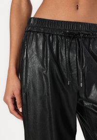 Zwarte neplederen broek met een elastische tailleband, koordsluiting en zijzakken met rits. Gladde textuur met een glanzende afwerking.