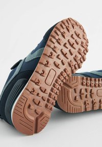 Mörkblå sneakers med grå detaljer, med en strukturerad gummisula med ett djupt mönster för grepp och en kardborrebandstängning.
