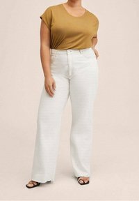 Haut léger de couleur moutarde avec des manches courtes, associé à un jean en denim blanc à taille haute et jambes larges. Sandales à talons blocs noires.