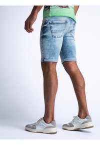 Pantalones cortos de mezclilla en un lavado claro con un aspecto desgastado, bajos doblados y dos bolsillos traseros; combinados con zapatillas grises y blancas.
