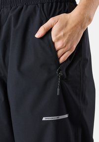 Black outdoor pants with elastic waistband, zippered pocket, smooth texture, and a reflective "SWEDEMOUNT" logo on the side.