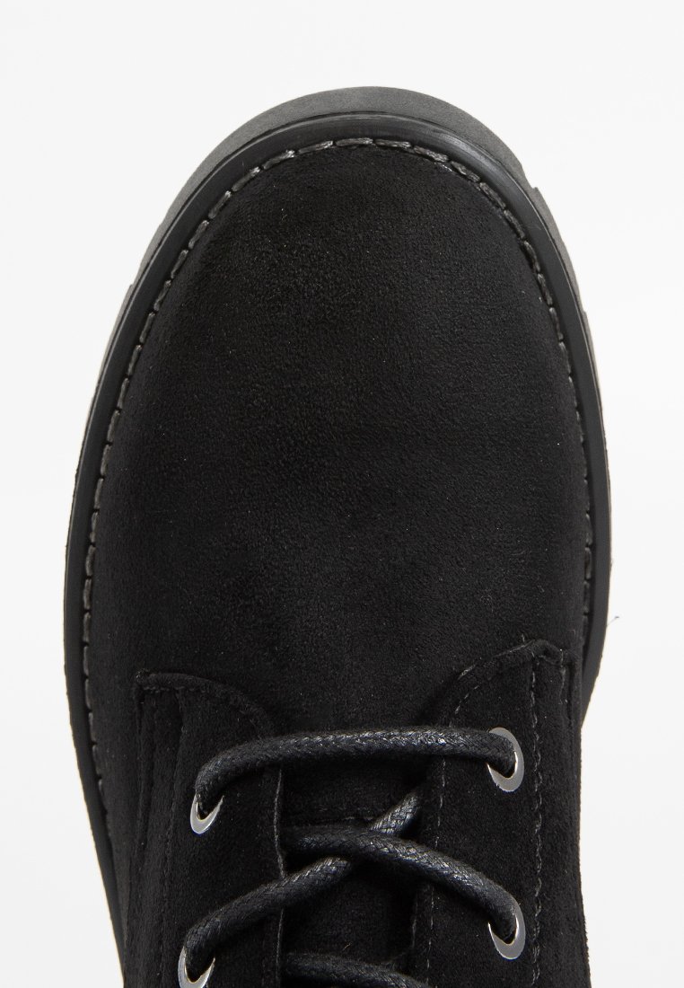 Botín de ante negro con punta redonda, diseño de cordones, costuras reforzadas y superficie texturizada. Suela de goma visible en el borde.