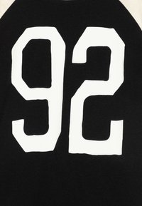 Schwarzer Textilstoff mit großen weißen Zahlen "92", die auffällig präsentiert werden. Die Zahlen sind in einer fetten Blockschrift mit einer strukturierten Oberfläche gestaltet.