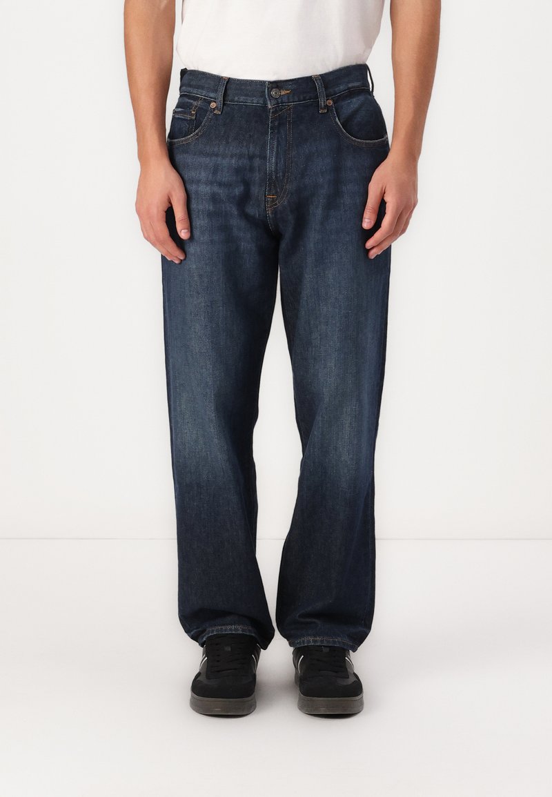 Tumedat sinised denim püksid, lõdva istuvusega, viie taskuga disain, nähtavad õmblused ning nupuga ja tõmblukuga kinnitamine vööl.