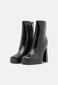 Botine negre cu toc înalt, realizate dintr-un material strălucitor, cu vârf rotund, fermoar pe lateral și talpă-platformă pentru un plus de înălțime.