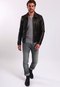 Černá kožená bunda se zipem, šedý svetr pod ní, světle modré džíny a černé kotníkové boty. Modelka stojící v uvolněné póze.