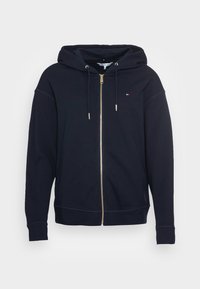 Felpa con zip di colore blu navy realizzata in tessuto morbido con cappuccio. Presenta una zip dorata, polsini a costine e un piccolo logo sul petto.
