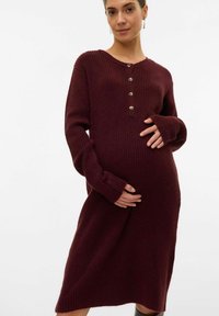 Ribana pletena trudnička haljina u boji maroon s okruglim izrezom, dugim rukavima i detaljima s gumbima na prsima, duljine do sredine lista.