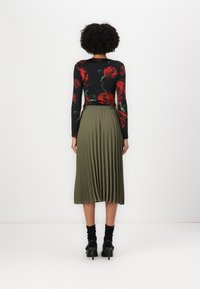 Maglietta a maniche lunghe con sfondo nero e stampa di rose rosse, abbinata a una gonna plissettata verde oliva e scarpe nere.