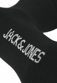 Schwarze Socke mit glatter Textur, auf der die Worte "JACK & JONES" in weißer Farbe an der Seite gestrickt sind.