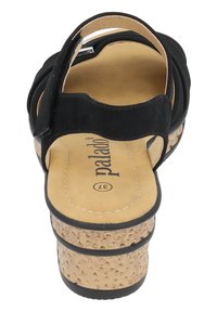 Sandalias negras con suela de cuña de corcho, con un upper suave, parte trasera abierta y plantilla acolchada. El diseño incluye detalles de tiras en forma curva.