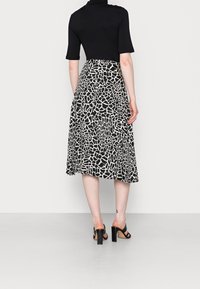 Schwarz Oberteil mit kurzen Ärmeln, kombiniert mit einem Midirock im weißen Giraffenmuster. Schwarze offene High Heels.
