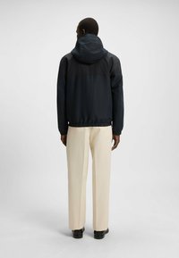 Chaqueta cortavientos de color navy con capucha, cintura elástica y mangas largas; textura suave; vista trasera que muestra un diseño minimalista.